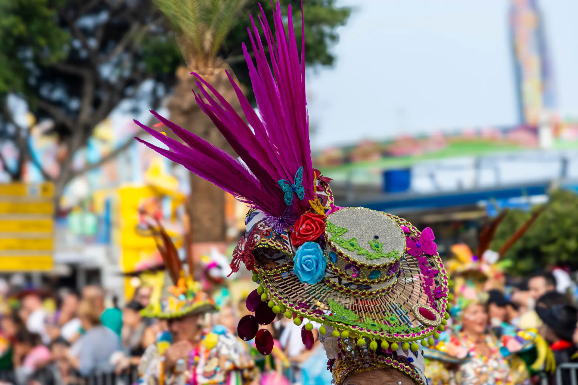 Close-up of an elaborate, colorful carnival hat decorated with bright purple feathers, artificial flowers, and beadwork during the festival in Tenerife, Spain.