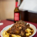 Close-up of a traditional Spanish oxtail stew (cola de toro) served with french fries on a white oval plate at Sol y Sombra in Seville, Spain