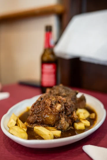 Close-up of a traditional Spanish oxtail stew (cola de toro) served with french fries on a white oval plate at Sol y Sombra in Seville, Spain