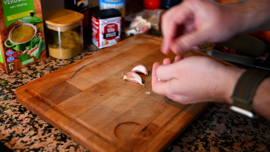 Close-up of hands peeling garlic cloves on a wooden cutting board while preparing the garbanzos con espinacas recipe for Tapas Hunters.