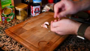 Close-up of hands peeling garlic cloves on a wooden cutting board while preparing the garbanzos con espinacas recipe for Tapas Hunters.
