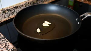 Close-up of garlic cloves frying in olive oil in a black pan on a stovetop during step 2 of the garbanzos con espinacas recipe for Tapas Hunters