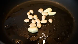 Close-up of peeled almonds and garlic cloves frying together in oil in a black skillet during step 3 of the garbanzos con espinacas recipe for Tapas Hunters.