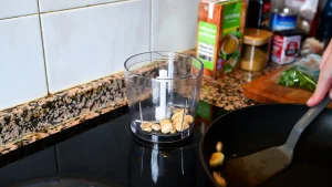 Close-up of transferring fried garlic and almonds from a pan into a small food processor bowl during step 4 of the garbanzos con espinacas recipe for Tapas Hunters.