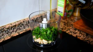 Close-up of adding fresh parsley and pouring olive oil into a food processor with garlic and almonds during step 5 of the garbanzos con espinacas recipe for Tapas Hunters.