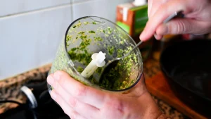 Close-up of hands mixing the blended garlic, almond, and parsley paste inside a food processor bowl during step 6 of the garbanzos con espinacas recipe for Tapas Hunters.