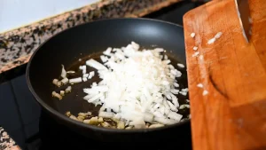 Close-up of transferring chopped onions from a wooden cutting board into a pan with hot oil during step 7 of the garbanzos con espinacas recipe for Tapas Hunters.