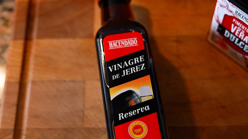 Close-up of a bottle of Hacendado Sherry Vinegar (Vinagre de Jerez Reserva) on a wooden surface during step 11 of the garbanzos con espinacas recipe for Tapas Hunters.