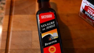 Close-up of a bottle of Hacendado Sherry Vinegar (Vinagre de Jerez Reserva) on a wooden surface during step 11 of the garbanzos con espinacas recipe for Tapas Hunters.