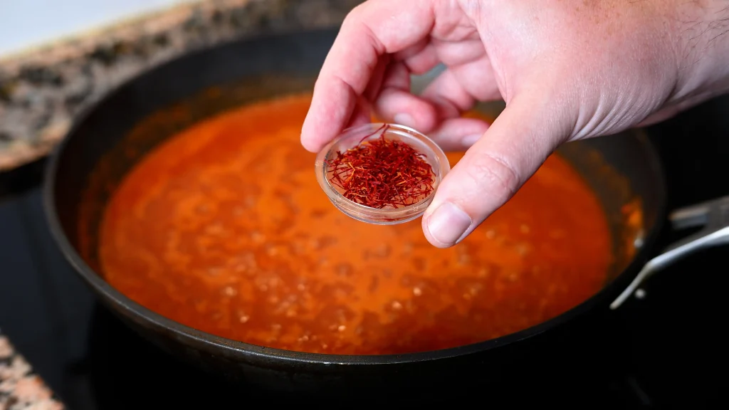Close-up of holding a small dish of saffron threads above a simmering pan during step 13 of the garbanzos con espinacas recipe for Tapas Hunters.