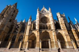 Low-angle view of the ornate Gothic facade, towers, and intricate rose window of the León Cathedral under a clear blue sky in Spain.