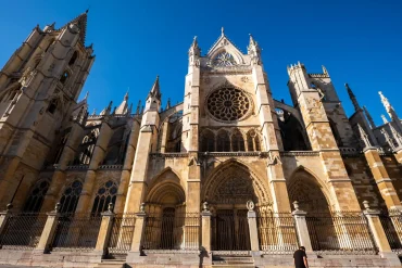 Low-angle view of the ornate Gothic facade, towers, and intricate rose window of the León Cathedral under a clear blue sky in Spain.