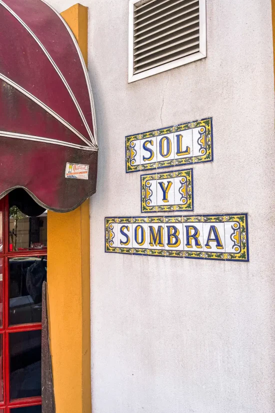 Close-up of traditional painted ceramic tile signage reading "Sol y Sombra" mounted on the exterior wall next to the entrance in Seville, Spain.